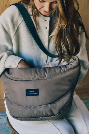 Woman seated and reaching into the Osma stroller organiser in Mocha worn across the front of her body