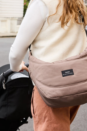 Woman wearing the Osma stroller organiser in Mocha across her body, seen from behind while she pushes a stroller