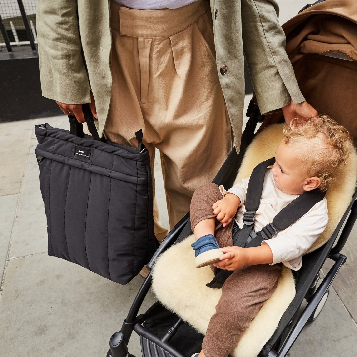Person pushing a stroller with a child sitting inside, holding a black bag.