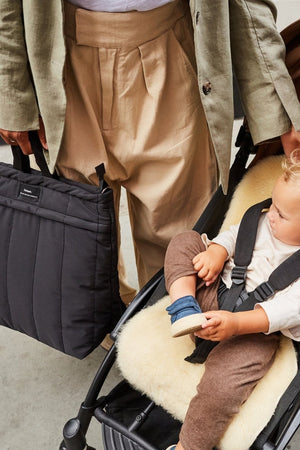 Person pushing a stroller with a child sitting inside, holding a black bag.