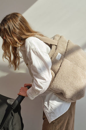Sigrid Eco Changing Bag beige worn over the shoulder by a woman leaning over to hold a pram handle