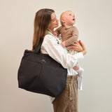 Sigrid Eco Changing Bag black, worn on the shoulder by a woman holding a baby who looks upwards