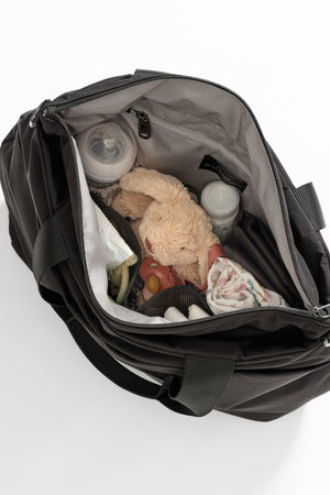 Sigrid Eco Changing Bag black, open from above showing a soft toy, bottles, dummy and muslin inside