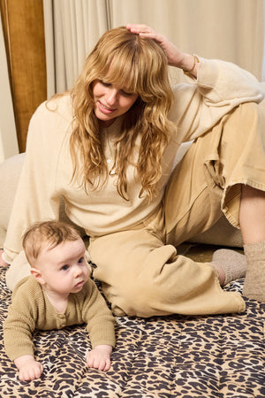 Thoren Eco Playmat in Leopard with a baby on tummy looking ahead while a woman sits beside them, soft toy at the edge