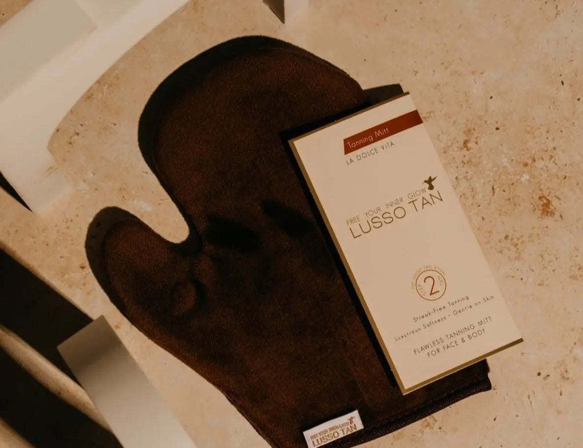 Flawless Tanning Mitt in brown, laid flat on stone with its Lusso Tan box resting on top