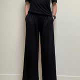 Person wearing a black outfit with wide-leg pants against a plain background