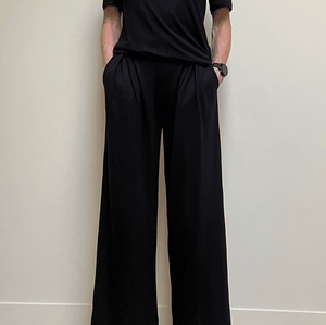 Person wearing a black outfit with wide-leg pants against a plain background