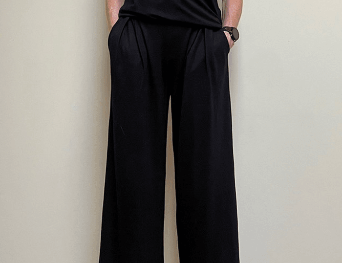 Person wearing a black outfit with wide-leg pants against a plain background