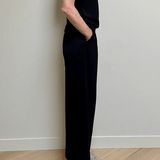Person wearing a black outfit standing against a white wall on a wooden floor.