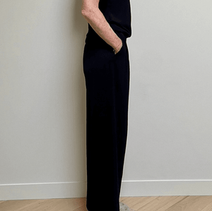 Person wearing a black outfit standing against a white wall on a wooden floor.