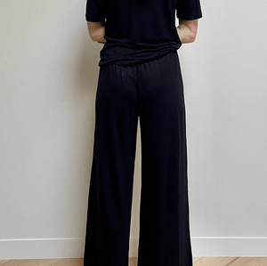 Person wearing a black outfit standing against a plain wall.