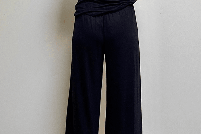 Person wearing a black outfit standing against a plain wall.