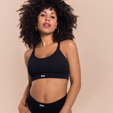 Woman wearing a black sports bra and leggings with 'Leash' branding on a beige background
