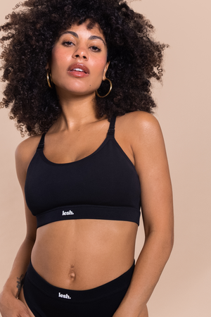 Woman wearing a black sports bra and leggings with 'Leash' branding on a beige background