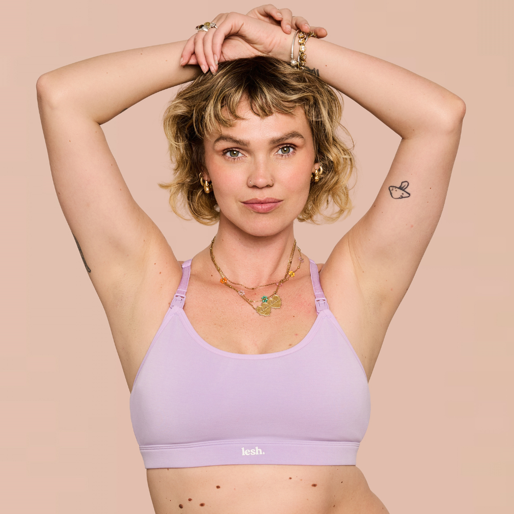 A woman with short blonde hair poses in a lavender sports bra against a solid beige background. The brand name 'kesh.