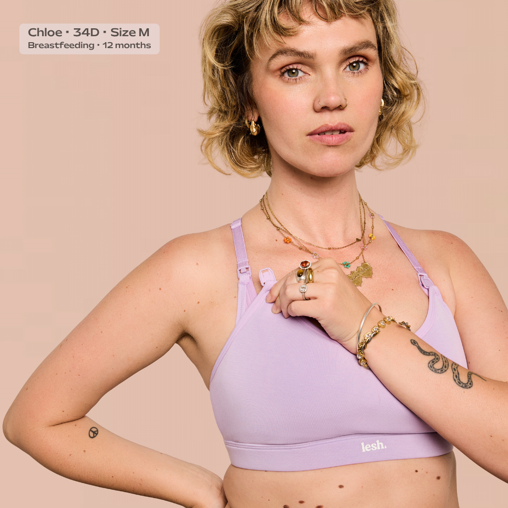 A woman modeling a light purple/lavender lace-up sports bra against a solid pale pink background. The brand name 'leash.