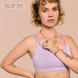 A woman modeling a light purple/lavender lace-up sports bra against a solid pale pink background. The brand name 'leash.