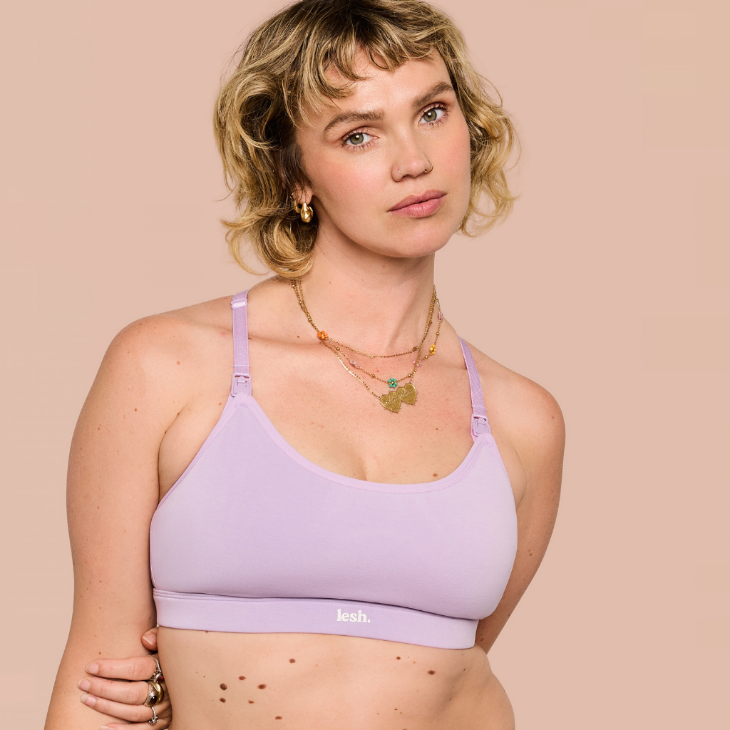 A woman modeling a light purple/lavender bralette with thin straps and a wide underband, shown against a solid pale peach background. The brand name 'kohl.