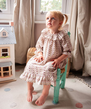 Beatrice Rose Stripe nightie, child sitting on a small green chair showing the ruffled collar, sleeves and hem