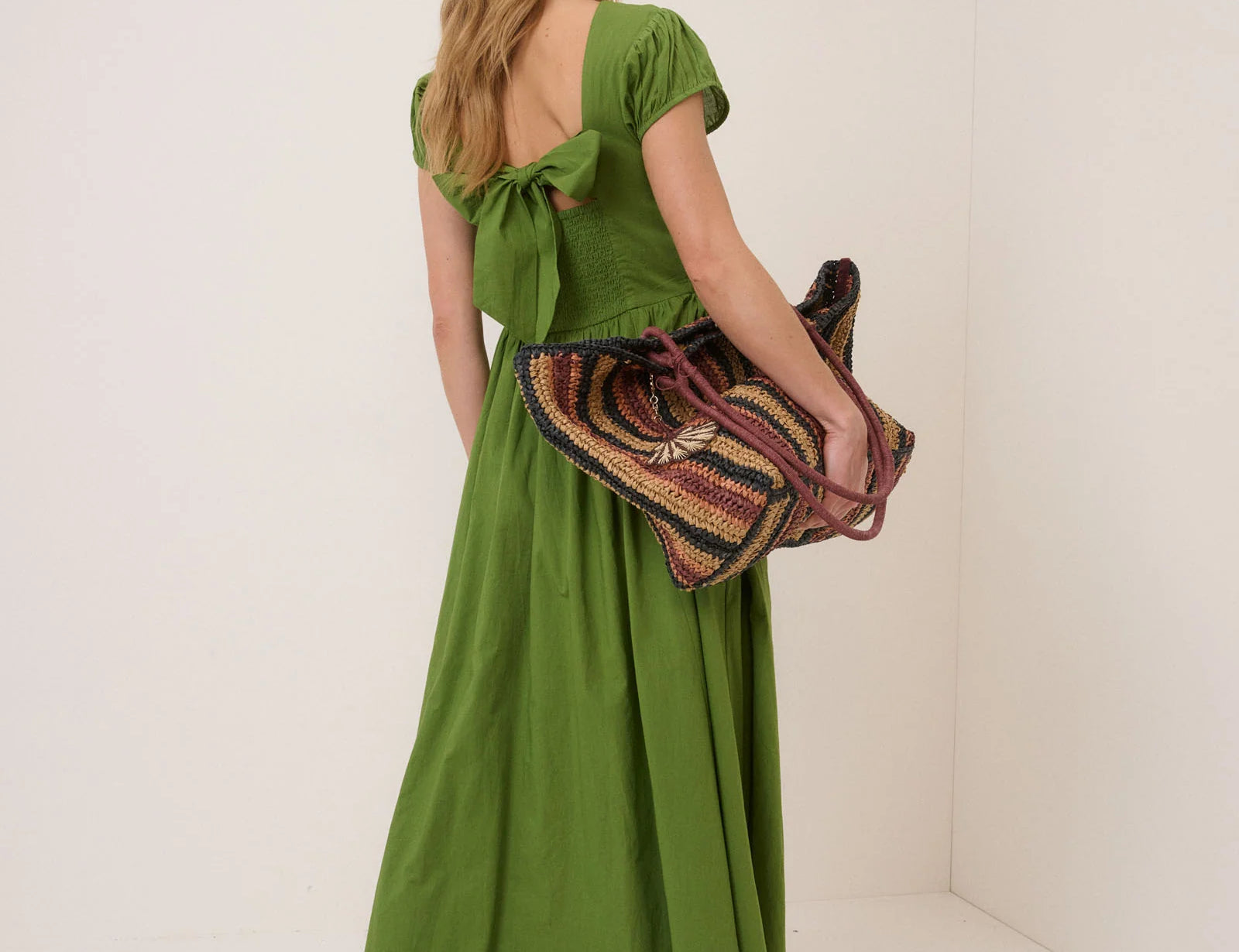 Woman in a green dress holding a patterned bag against a white background