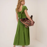 Woman in a green dress holding a patterned bag against a white background