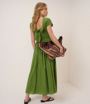 Woman in a green dress holding a patterned bag against a white background