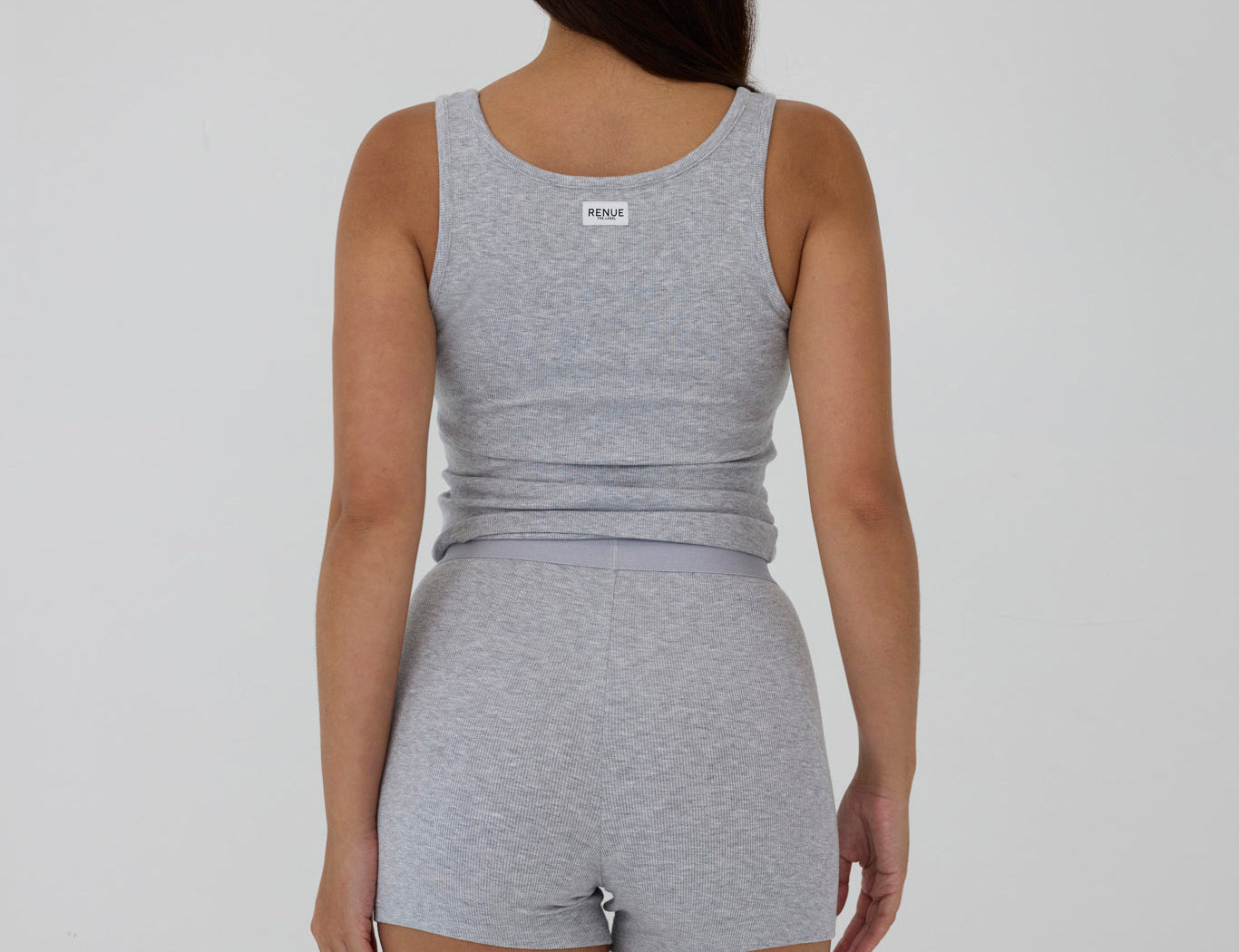 A woman shown from the back wearing a heather gray sleeveless tank top and matching high-waisted shorts against a plain light gray studio background.