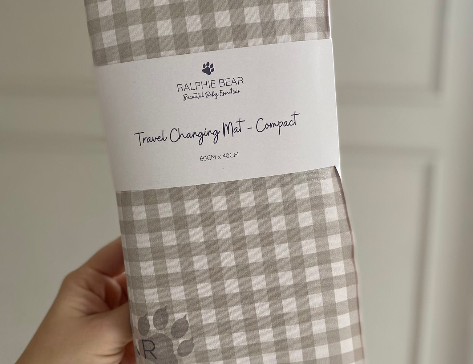 Checkered travel changing mat with Ralphie Bear branding held by a hand against a neutral background