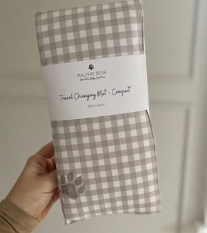Checkered travel changing mat with Ralphie Bear branding held by a hand against a neutral background