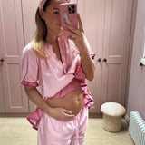 Woman in pink pajama set taking a mirror selfie in a room with pink walls.