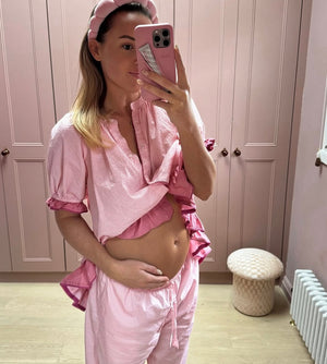 Woman in pink pajama set taking a mirror selfie in a room with pink walls.