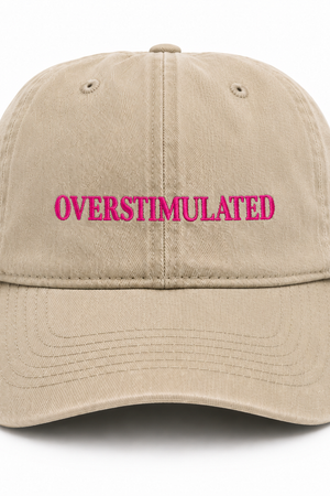 Beige cap with 'OVERSTIMULATED' in pink text on a white background
