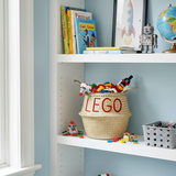 LEGO belly basket, large, on a white shelf filled with toy bricks, beside books, a rocket print and a toy robot