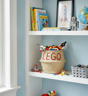 LEGO belly basket, large, on a white shelf filled with toy bricks, beside books, a rocket print and a toy robot