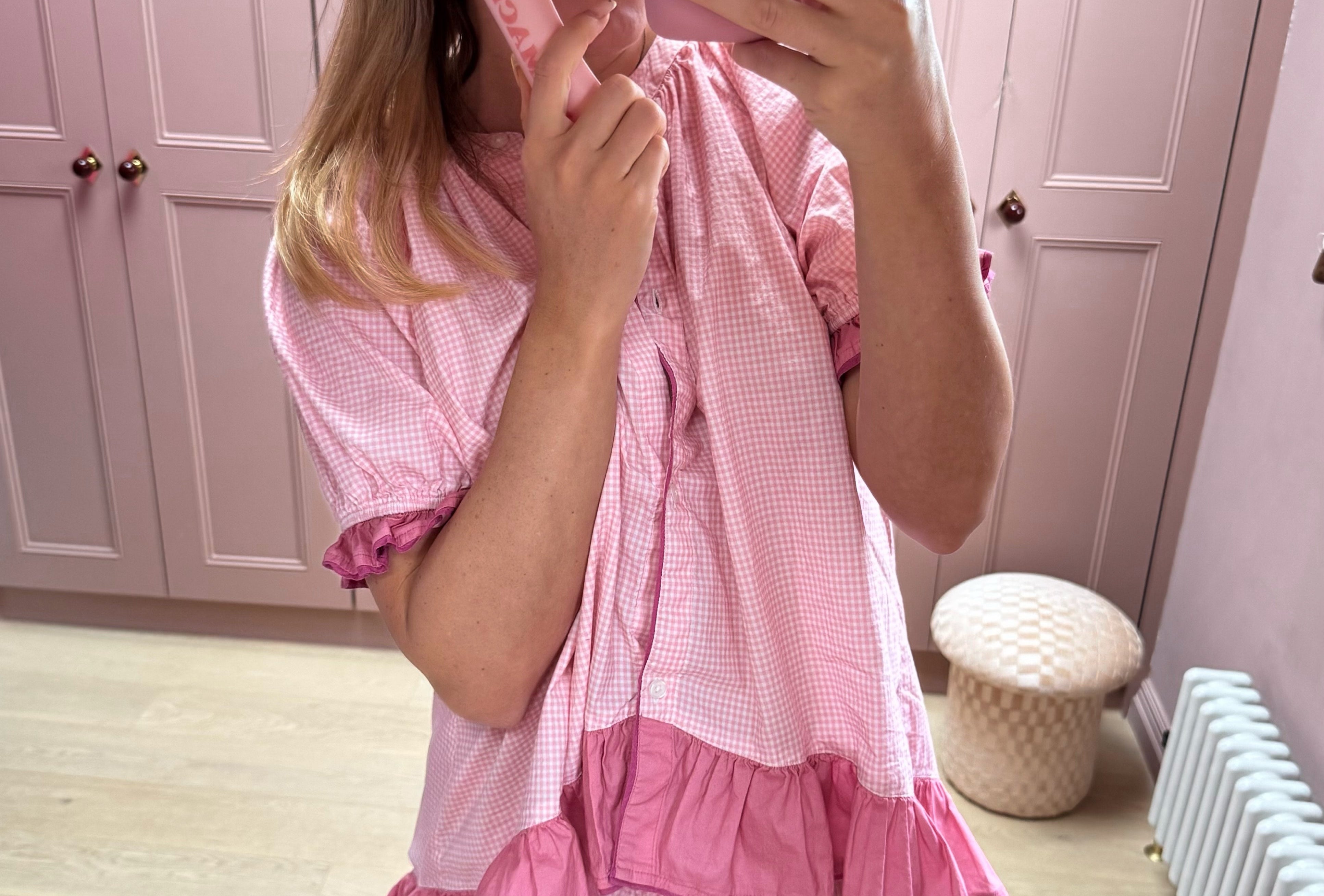 Person wearing a pink outfit with matching headband and phone case in a room with pink walls.