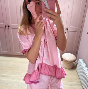 Person wearing a pink outfit with matching headband and phone case in a room with pink walls.
