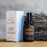 Calm Room Spray bottle standing beside its box in front of dried lavender on a wooden surface