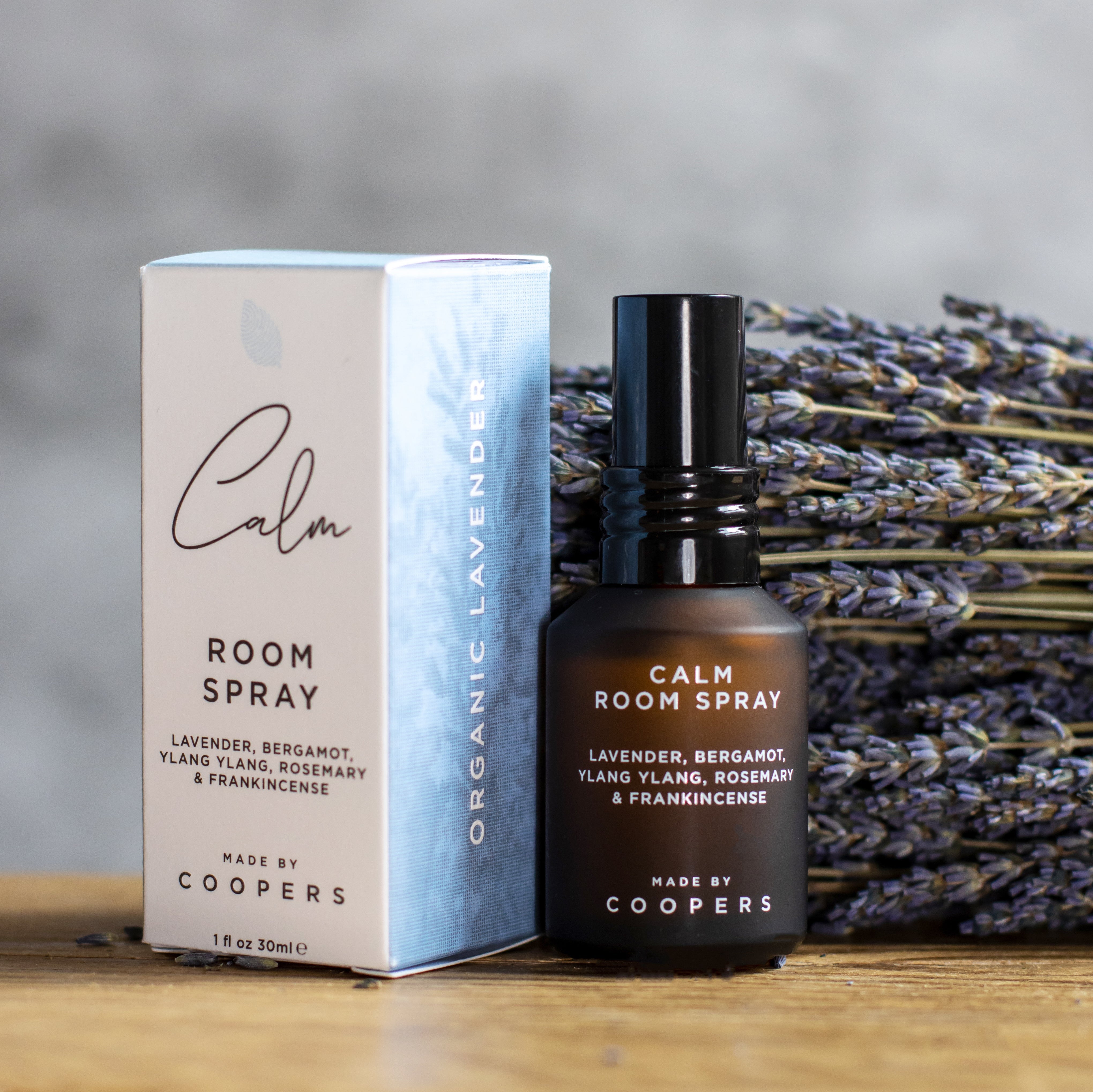 Calm Room Spray bottle standing beside its box in front of dried lavender on a wooden surface