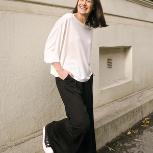 Woman in a white top and black pants standing against a light-colored building.