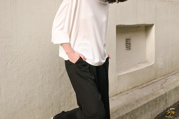 Woman in a white top and black pants standing against a light-colored building.