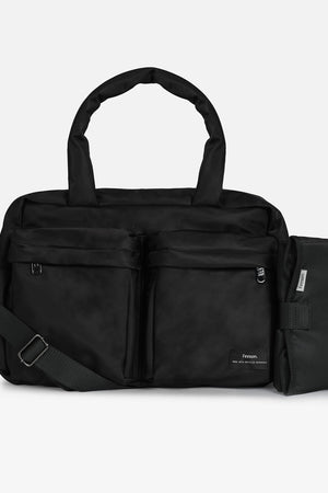 A black multi-compartment duffel bag with a detachable shoulder strap and an attached black pouch on the side, shown against a light gray background.