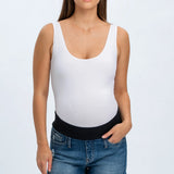 Woman wearing a white tank top and denim shorts on a plain background