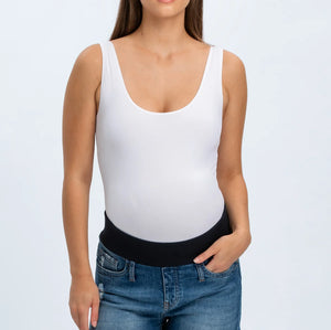 Woman wearing a white tank top and denim shorts on a plain background