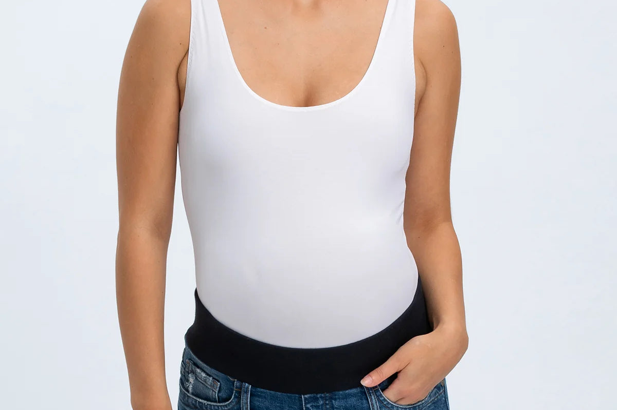 Woman wearing a white tank top and denim shorts on a plain background