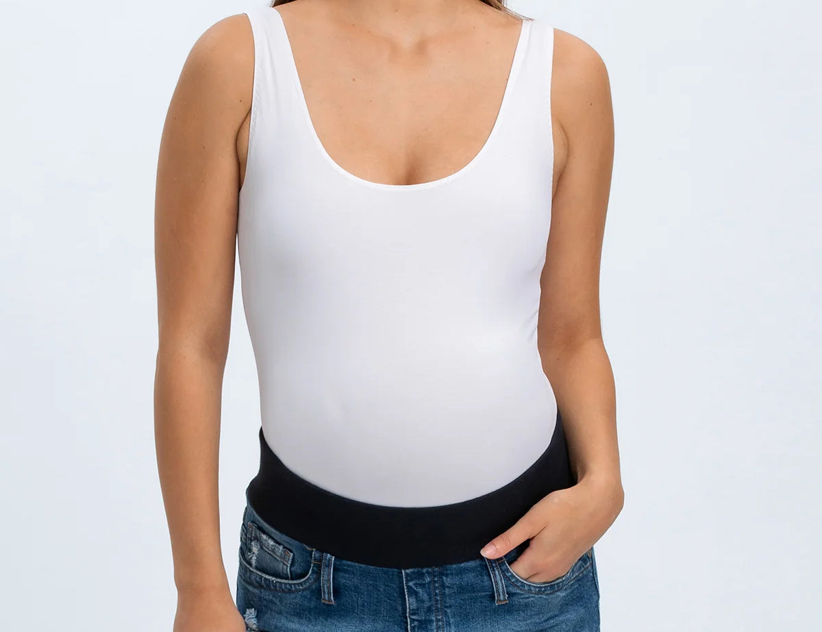 Woman wearing a white tank top and denim shorts on a plain background