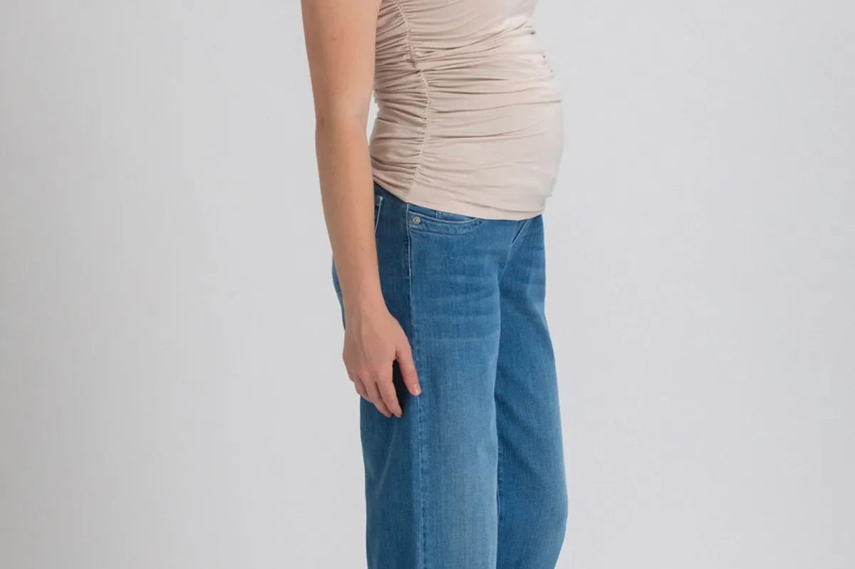 Woman wearing a beige top and blue jeans on a white background