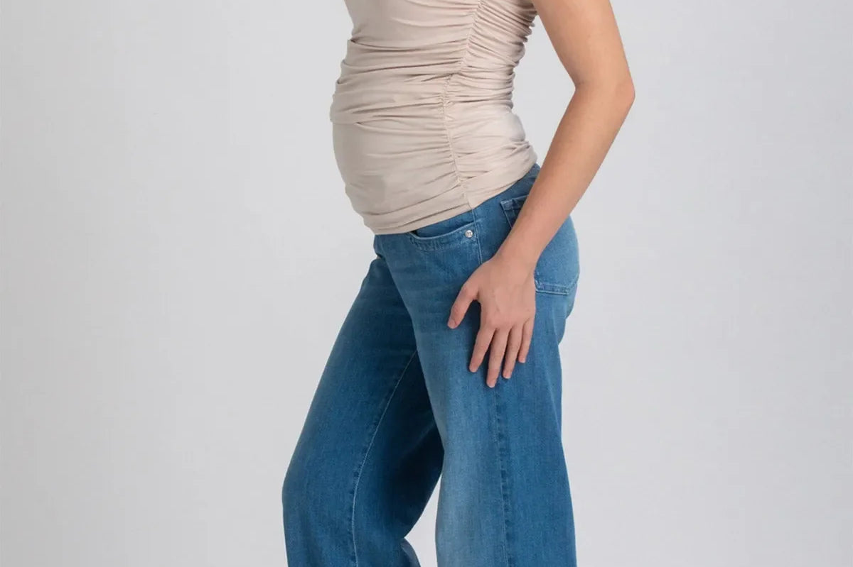 Woman wearing a beige sleeveless top and blue jeans on a white background