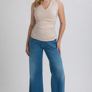 Woman wearing a beige sleeveless top and blue jeans on a white background
