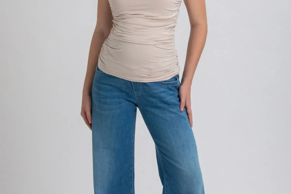 Woman wearing a beige sleeveless top and blue jeans on a white background
