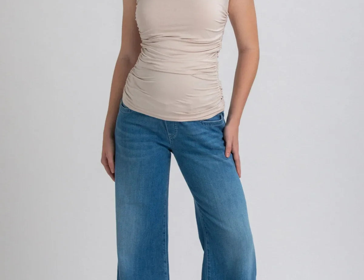 Woman wearing a beige sleeveless top and blue jeans on a white background